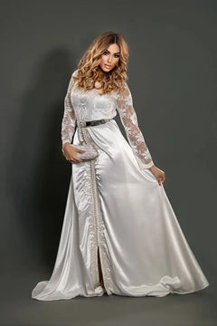 Witte Caftan Belissima van verfijnde kant met zilverkleurige ceintuur, elegante silhouet en luxe afwerkingen geïnspireerd op Marokkaans vakmanschap.