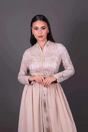 Zoom sur le buste d’un caftan beige à broderies sophistiquées et finitions artisanales, mettant en valeur les détails du tissu et de la coupe.
