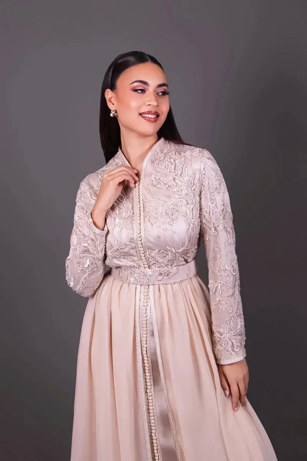 Dettaglio della parte superiore di un caftano marocchino beige ricamato, con maniche lunghe, collo raffinato e cintura elegante, indossato da un manichino.