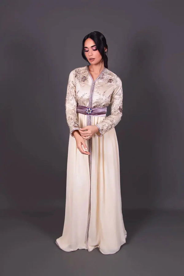 Modèle portant le caftan marocain MODE & CAFTAN Sameera crème avec broderies délicates et ceinture mauve satinée